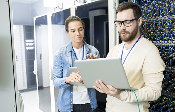 Two individuals standing in front of a server, discussing technology and data management.