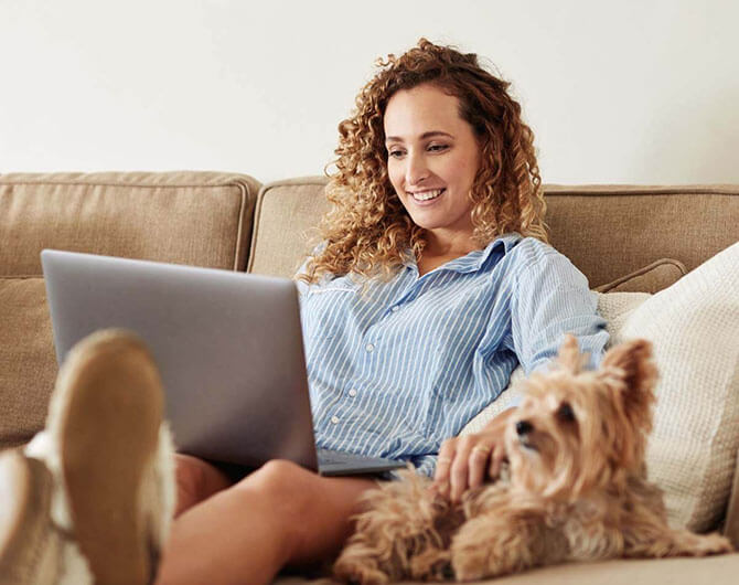 Woman looking at her laptop with dog next to her
